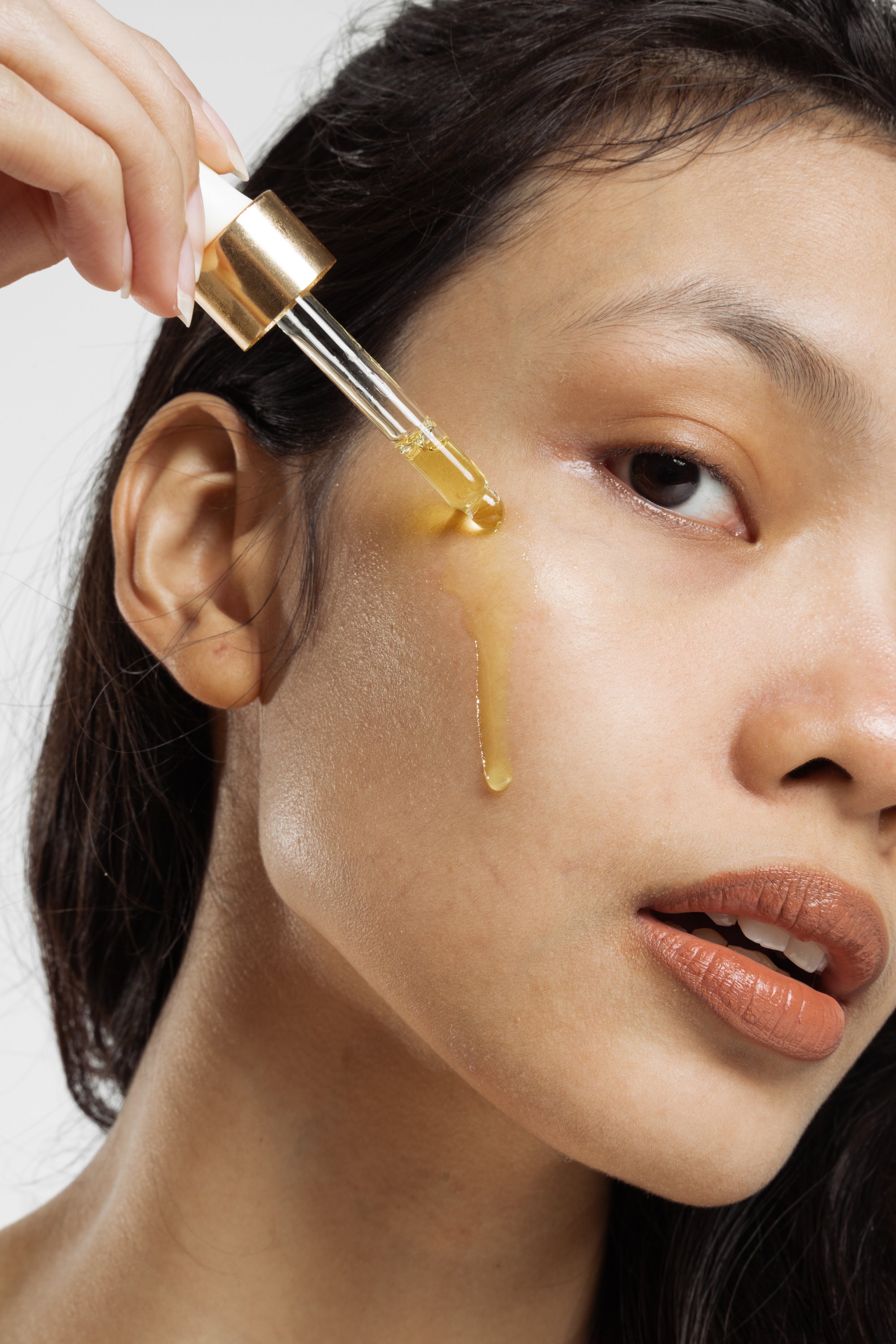 Closeup Portrait of Woman Applying Oil on Face with Dropper